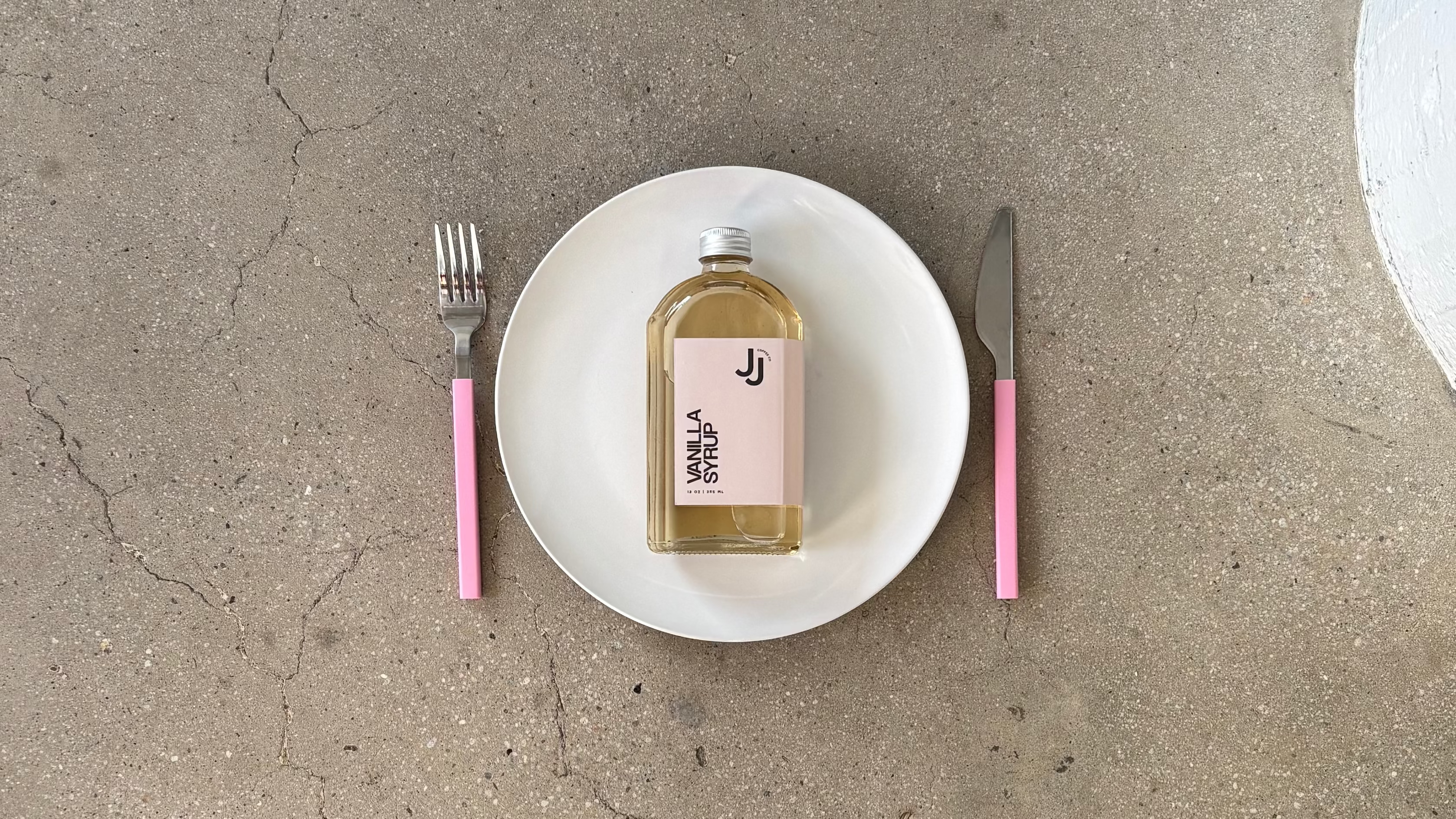 Concrete floor with a plate of syrup. bottle, fork, and knife.