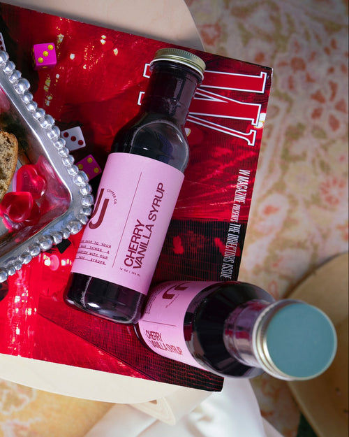 Bottle of cherry vanilla syrup on a magazine with a small loaf of bread and decorative hearts.